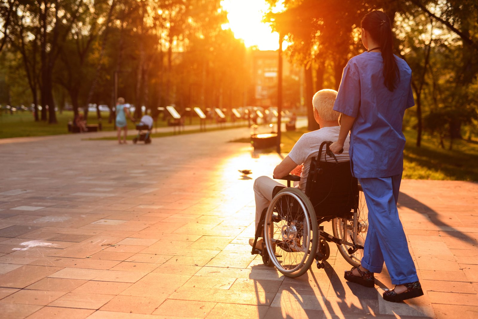 Old man in a wheelchair and a nurse are walking in the park